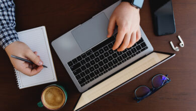 Man working at the laptop with a cup of coffee, phone, writing with pen at home