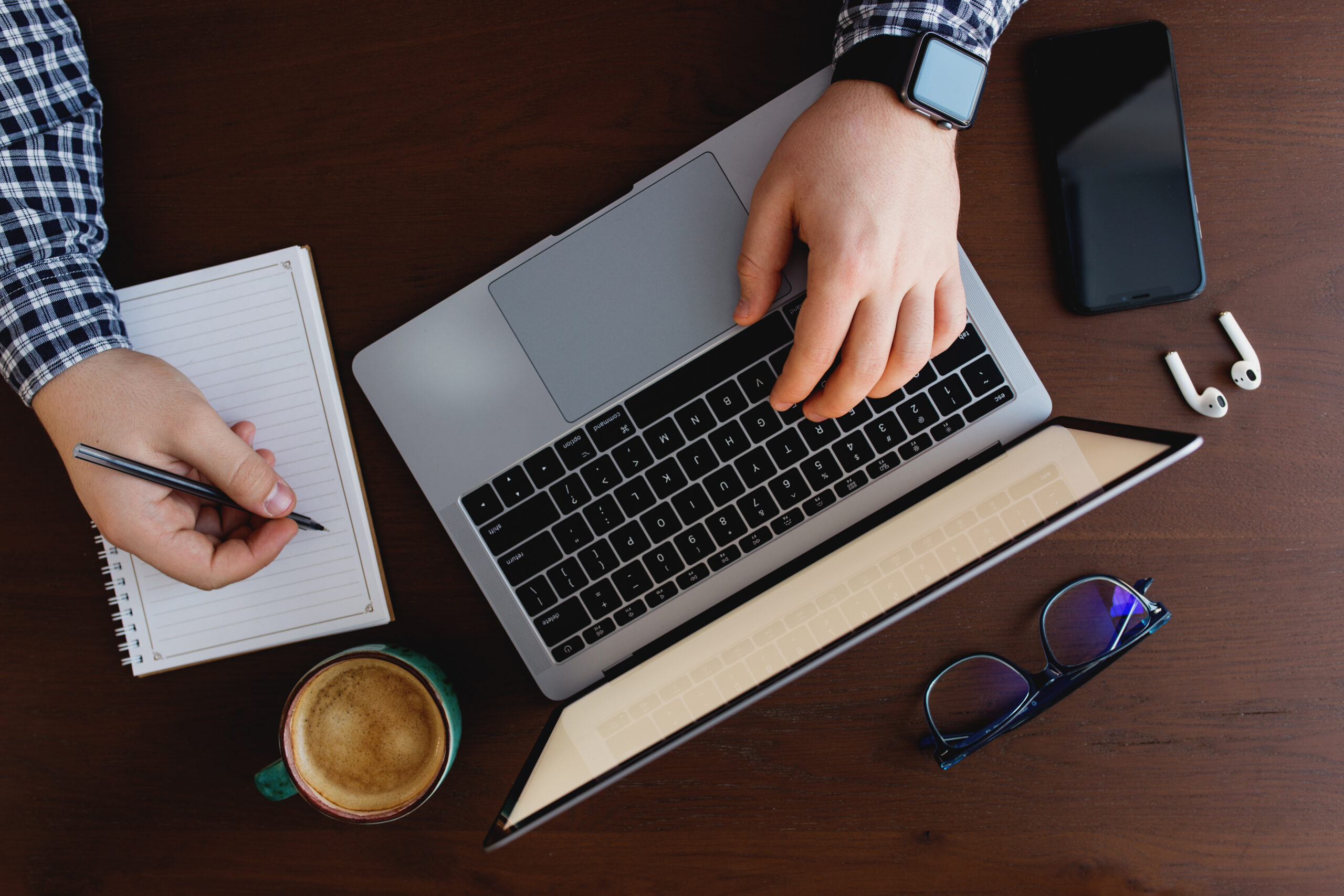 Man working at the laptop with a cup of coffee, phone, writing with pen at home